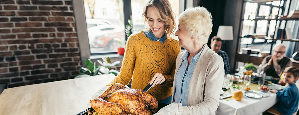 Image of senior woman and adult woman talking while carving a turkey